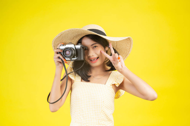 A beautiful, happy woman wearing a big hat and a camera on a yellow background. - Valokuva, kuva