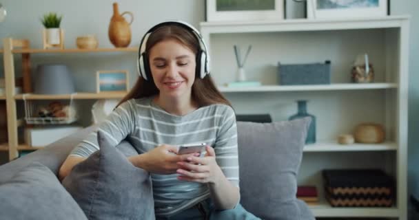 Beautiful young woman is listening to music with headphones using smartphone - Video, Çekim