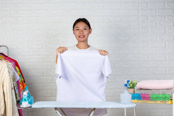 A young maid who is preparing a shirt on her ironing board with a white brick background. - Photo, image