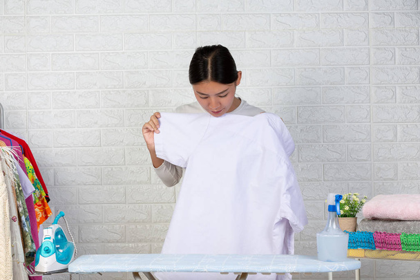 A young maid who is preparing a shirt on her ironing board with a white brick background. - Foto, Imagem