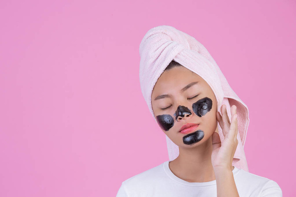 Schoonheid cosmetische peeling. Jonge vrouw met zwarte peel off masker op de huid cosmetische huidverzorging peeling product op gezicht op een roze achtergrond. - Foto, afbeelding