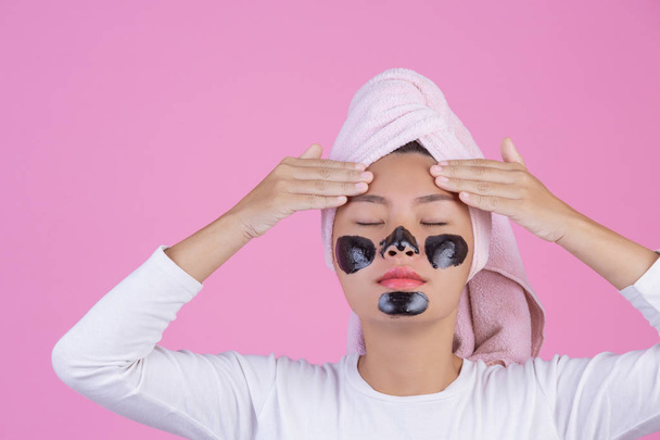 Beauty cosmetic peeling. Young female with black peel off mask on skin cosmetic skin care peeling product on face on a pink background. - Foto, imagen