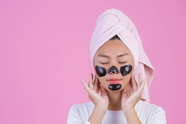 Beauty cosmetic peeling. Young female with black peel off mask on skin cosmetic skin care peeling product on face on a pink background. - 写真・画像