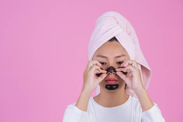 Beauty cosmetic peeling. Young female with black peel off mask on skin cosmetic skin care peeling product on face on a pink background. - Foto, imagen