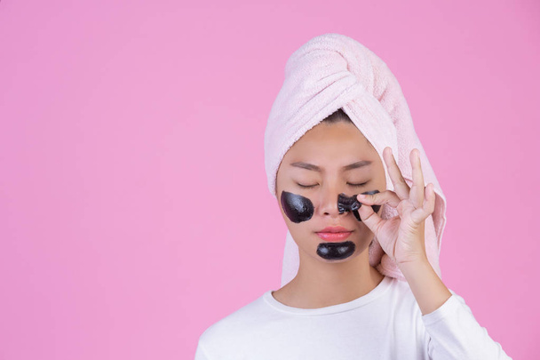 Kozmetikai hámlás. Fiatal nő fekete lehúzható maszk a bőr kozmetikai bőrápolás peeling termék arcon rózsaszín alapon. - Fotó, kép