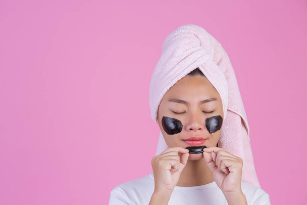 Beauty cosmetic peeling. Young female with black peel off mask on skin cosmetic skin care peeling product on face on a pink background. - Foto, Imagen