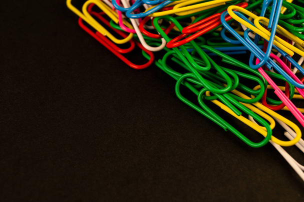 Many colorful paper clips lie on a black background paper - Photo, image