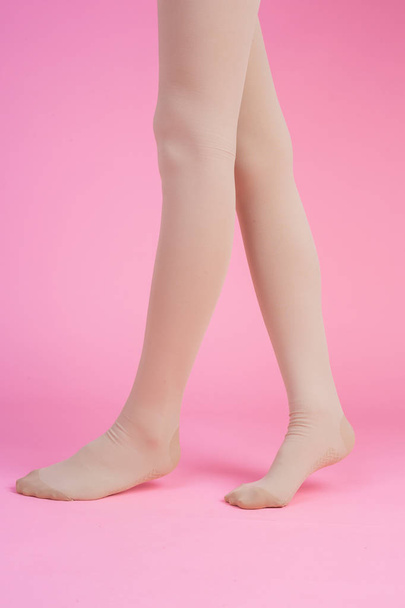 Slender legs, beautiful woman wearing stockings standing on a pink background. - Фото, изображение