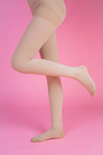 Slender legs, beautiful woman wearing stockings standing on a pink background. - Foto, imagen