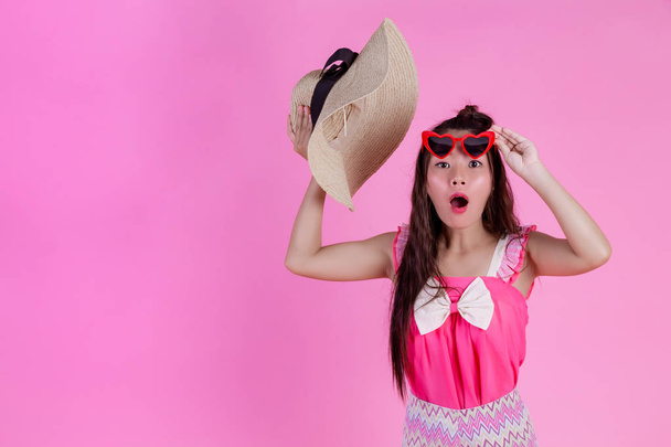 A beautiful woman wearing red glasses with a big hat on a pink background. - 写真・画像