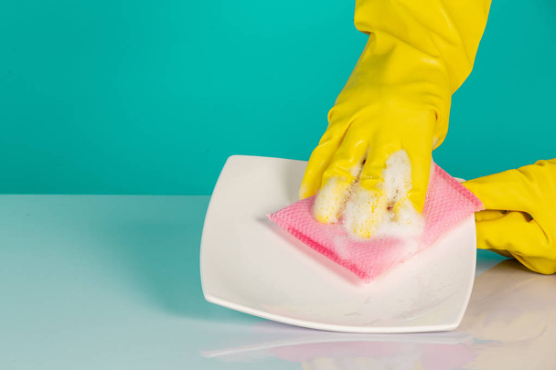 El concepto de lavavajillas con guantes amarillos sobre un fondo azul. - Foto, Imagen