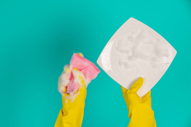 El concepto de lavavajillas con guantes amarillos sobre un fondo azul. - Foto, imagen