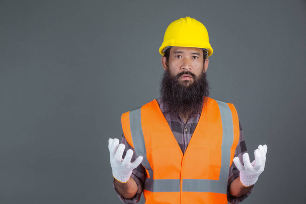 Een ingenieur met een gele helm met witte handschoenen... toonde een gebaar op een grijze achtergrond.. - Foto, afbeelding