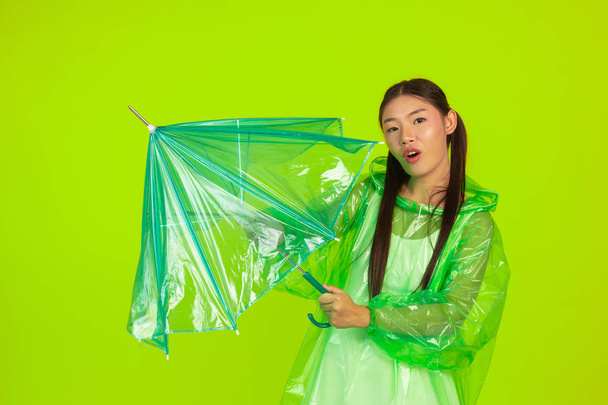 Ragazza indossa un abito verde pioggia e tiene un ombrello pioggia su uno sfondo verde. - Foto, immagini