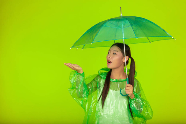 Dziewczyna nosi deszcz zielony strój i trzyma parasol deszcz na zielonym tle. - Zdjęcie, obraz