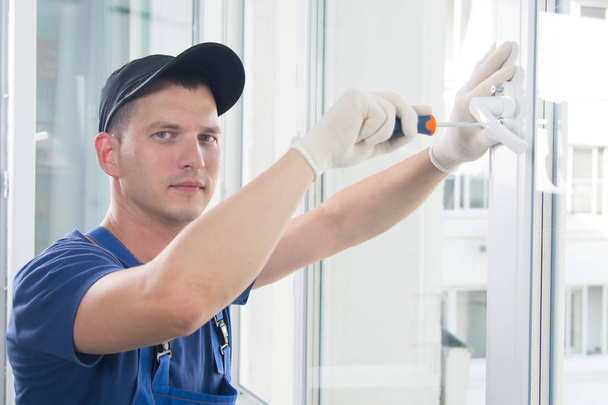 worker in blue uniform screwdriver handles the handle to the plastic window - Foto, Imagen