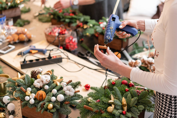 Glue gun in woman hand. Manufacturer of Christmas wreath from branches of pine for holiday. Master class on making decorative ornaments. - Photo, Image
