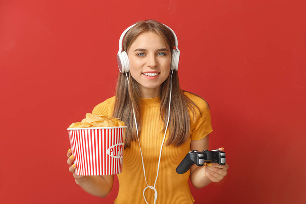 Tiener meisje met popcorn spelen videospel op kleur achtergrond - Foto, afbeelding