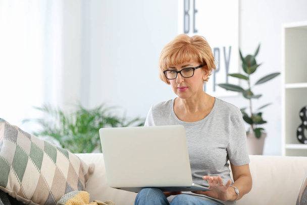 Beautiful middle-aged woman with laptop at home - Фото, зображення