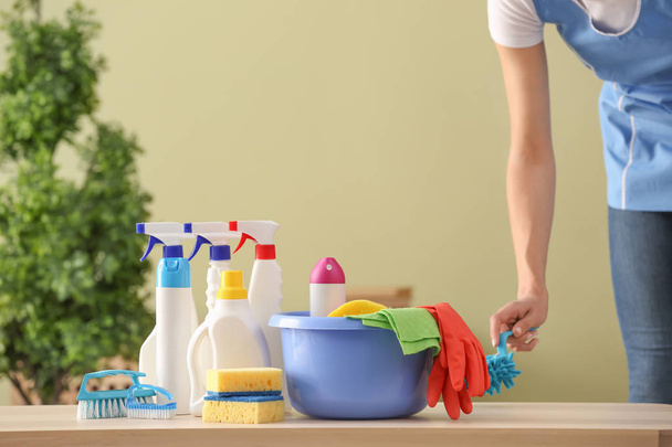 Mulher zeladora com suprimentos de limpeza na mesa no quarto
 - Foto, Imagem