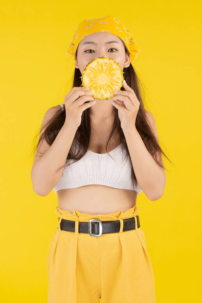Schöne Frau mit einer Ananas auf gelbem Hintergrund. - Foto, Bild