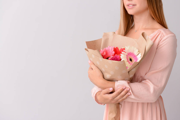 Mulher com buquê de belas flores de gerbera no fundo claro
 - Foto, Imagem