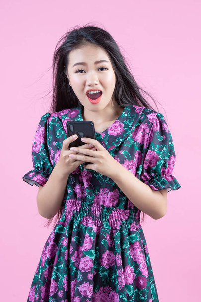 Девушка-подросток показывает телефон и эмоции лица на розовом фоне. - Фото, изображение