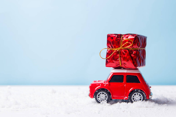Миниатюрная красная машинка, доставляющая подарочную коробку на синем фоне. Концепция рождественских открыток
. - Фото, изображение