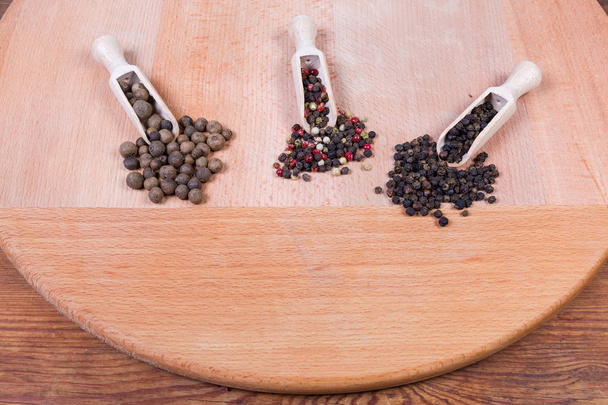 Varios granos de pimienta enteros en diferentes cucharas de especias de madera y al lado
 - Foto, imagen