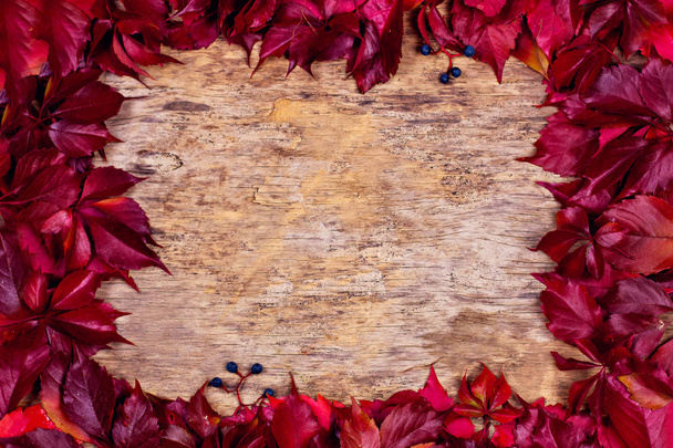 Červené podzimní listí na dřevěném pozadí. Rámeček podzimních listů. Texturované vinobraní rustikální dřevěné pozadí s podzimní červené listy. - Fotografie, Obrázek