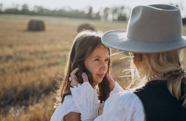 portrait of mother holding daughters hair standing in the field with straw bales  - Foto, afbeelding