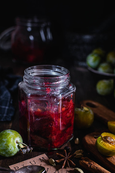 Homemade preserves, plum jam with spices in glass jar, dark wood - Zdjęcie, obraz
