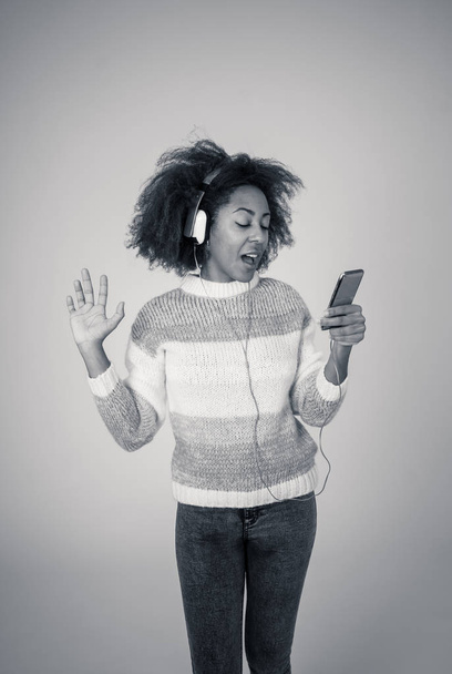Colorful portrait of gorgeous and happy african american woman listening to smart phone music app in headphones singing and dancing on neutral background. In people Music Technology and Happiness. - Photo, Image