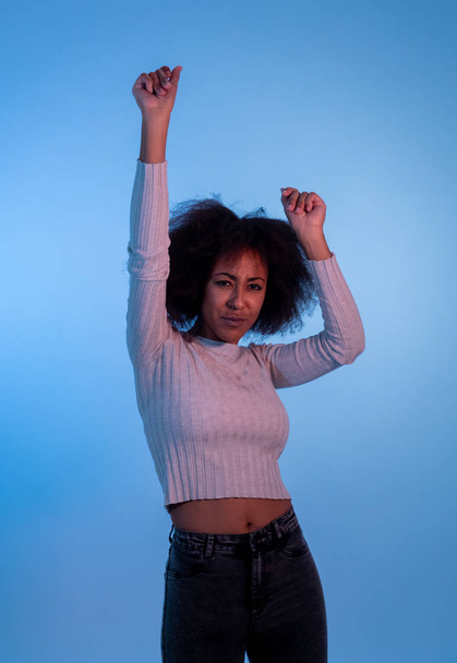 Portrait of inspired cool african american woman dancing feeling the music and enjoying life on blue moody disco light background. In People, Youth Party night lifestyle. Studio shot and copy space. - 写真・画像