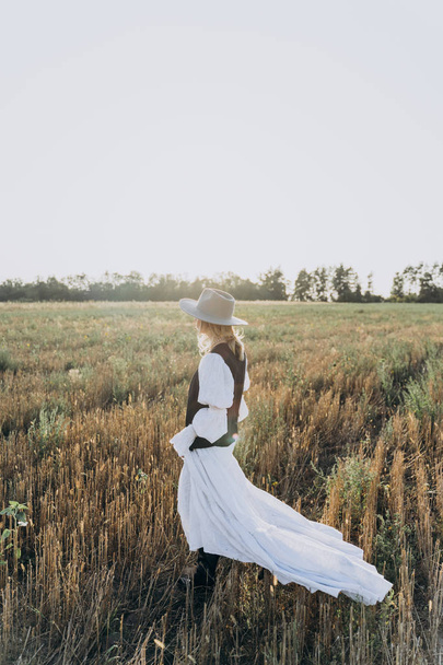side view of stylish woman in long white dress standing in the field  - 写真・画像