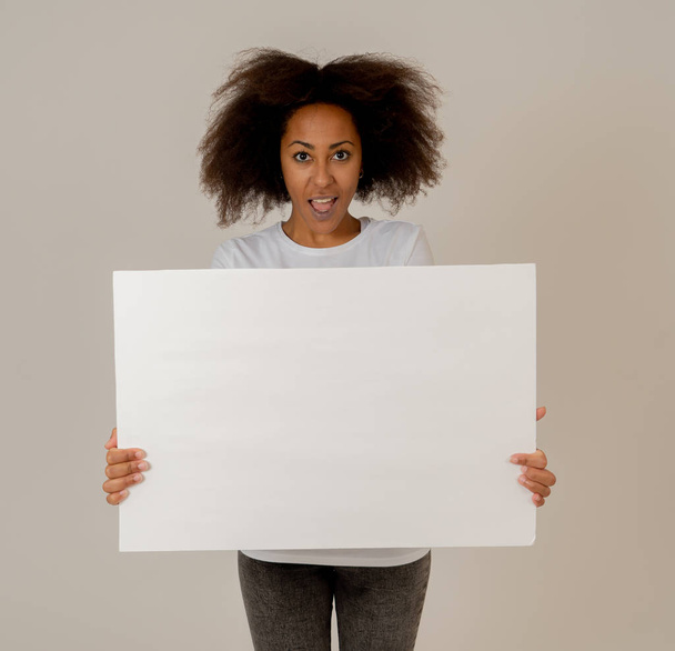 Αστεία και όμορφη αφρικανική Αμερικάνικη γυναίκα που δείχνει και δείχνει σε κενό πίνακα με χώρο αντιγραφής για το κείμενο. Φιλικό και ενθουσιασμένο γυναίκα με άφρο στυλ μαλλιών κρατώντας κενή αφίσα. Στην έννοια του μάρκετινγκ. - Φωτογραφία, εικόνα