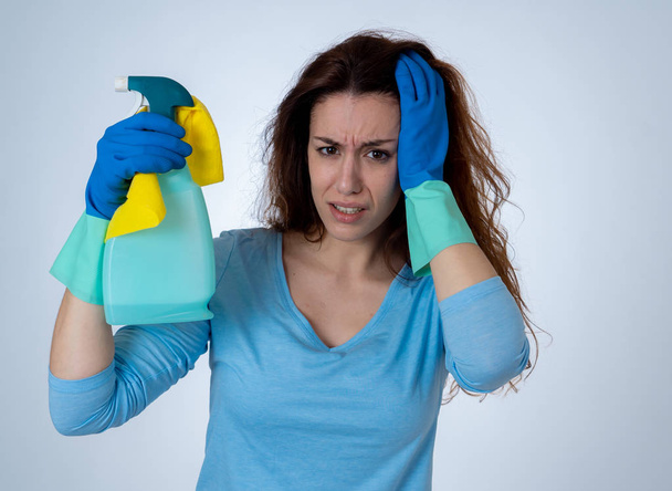 Young beautiful upset housewife woman holding bucket mop cleaning spray feeling stressed tired and frustrated in domestic duties and gender roles concept. Studio shot isolated on blue background. - Фото, изображение