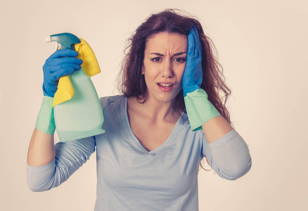 Young beautiful upset housewife woman holding bucket mop cleaning spray feeling stressed tired and frustrated in domestic duties and gender roles concept. Studio shot isolated on blue background. - Foto, imagen