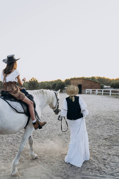 back view of girl riding horse while mother holding bridle and walking near on the ranch  - Foto, Imagem