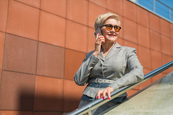 stylish woman in a suit and glasses against the background of a glass building phoning - Foto, Imagen