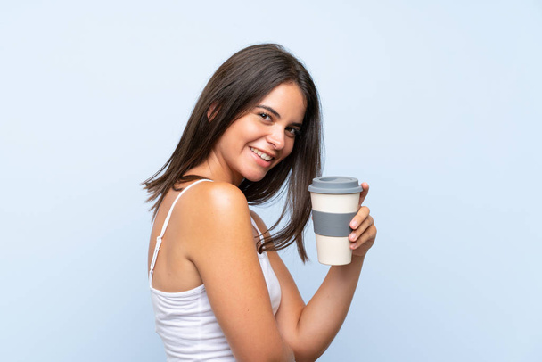 Молода жінка тримає каву на ізольованому синьому фоні
 - Фото, зображення