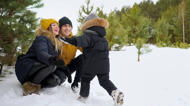 Little boy with a run rushes into the arms of his parents and drops them in the snow. - Photo, Image