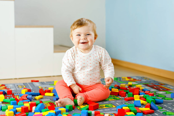 Urocza dziewczynka bawiąca się zabawkami edukacyjnymi. Szczęśliwe zdrowe dziecko bawiące się kolorowe różne drewniane klocki w domu w pokoju domowym. Baby uczenia się kolorów i form - Zdjęcie, obraz