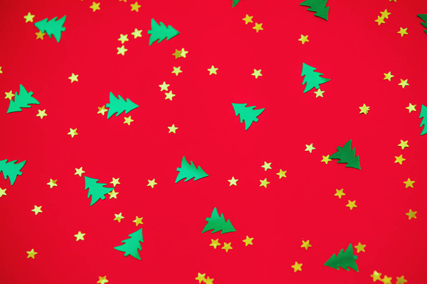 groene kerstbomen en gouden sterren confetti sparse op rood terug - Foto, afbeelding