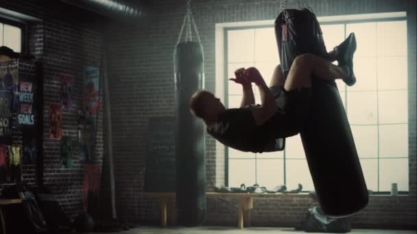Insane Punching Bag Crunches. Strong Masculine Man Embrassing the Bag with His Legs and Pumping His Abs and Core Muscles. Handsome Male Trains in a Gym with Motivational Posters. - Filmati, video