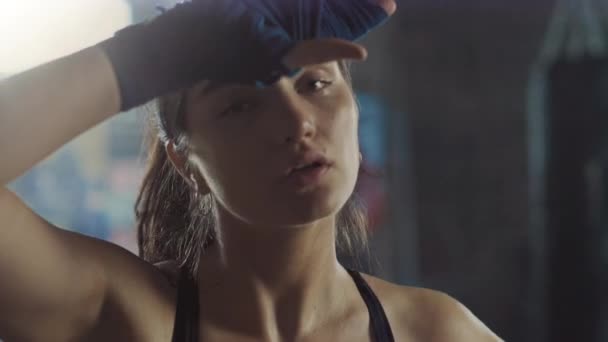 Portrait of a Beautiful Strong Fit Brunette Kickboxer Standing in a Loft Gym with Motivational Posters. She's Catching Her Breath after Intense Fitness Training Program. Athlete has Sweat on Her Face. - Filmati, video