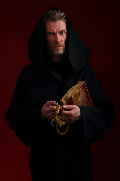 Medieval monk in black cassock with books and rosary - Fotoğraf, Görsel
