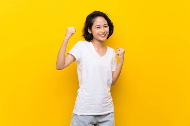 勝利を祝う孤立した黄色の壁の上にアジアの若い女性 - 写真・画像