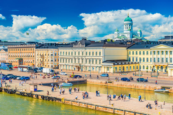 malerisches Stadtbild von Helsinki, Finnland. Blick auf die Innenstadt mit historischen Gebäuden, der Kathedrale, schönen Wolken am blauen Himmel und Menschen, die an einer Böschung entlang laufen - Foto, Bild