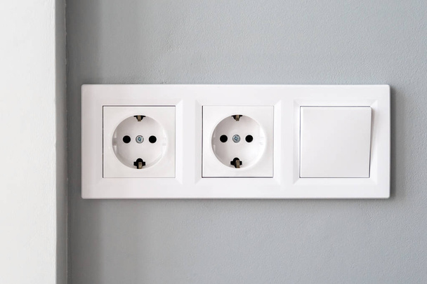 Vue rapprochée d'un groupe de prises électriques européennes blanches et d'un interrupteur situé sur un mur gris
 - Photo, image
